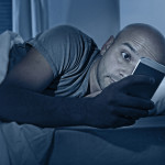 young cell phone addict man awake at night in bed using smartphone for chatting flirting and sending text message in internet addiction and mobile abuse concept